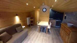 A wooden interior with a sofa, dining table, chairs, a clock, and a kitchen area.