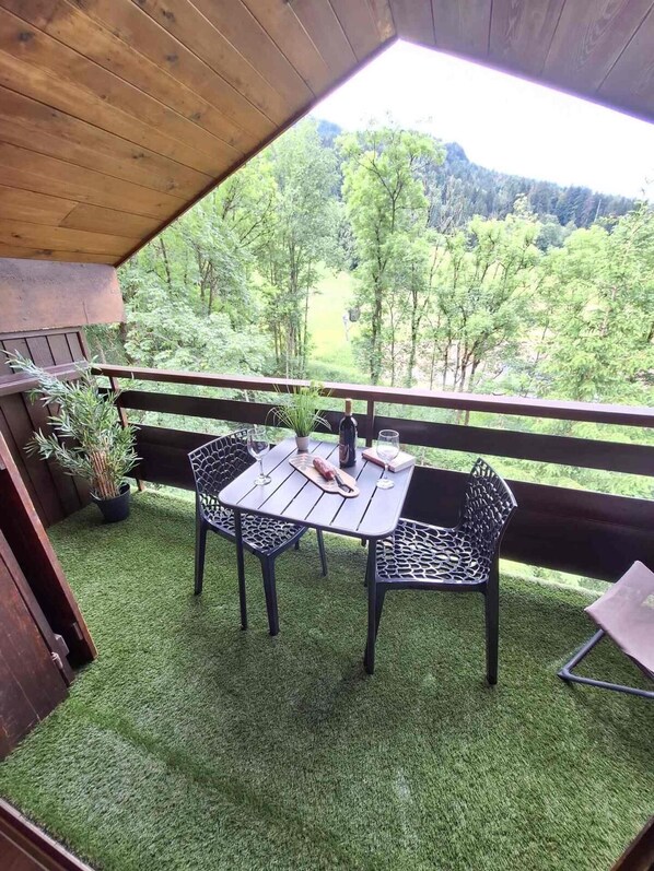 An outdoor patio with a table and chairs, surrounded by a wooden deck and a view of a forested landscape.