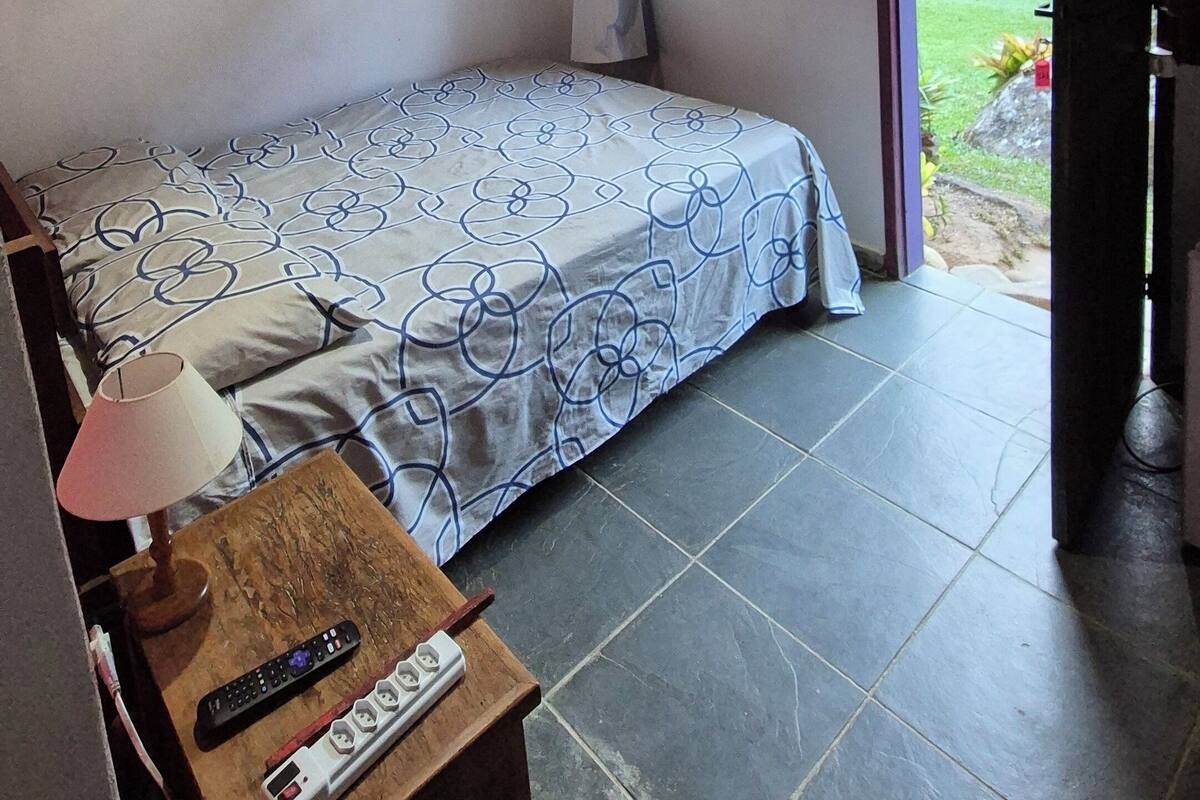 Un dormitorio con cama, escritorio, lámpara, televisor y ventana con vistas al exterior.
