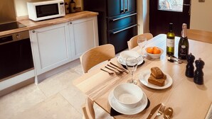 A modern kitchen with white cabinets, a black refrigerator, a microwave, and a dining table set with plates, cutlery, and a bottle of wine.