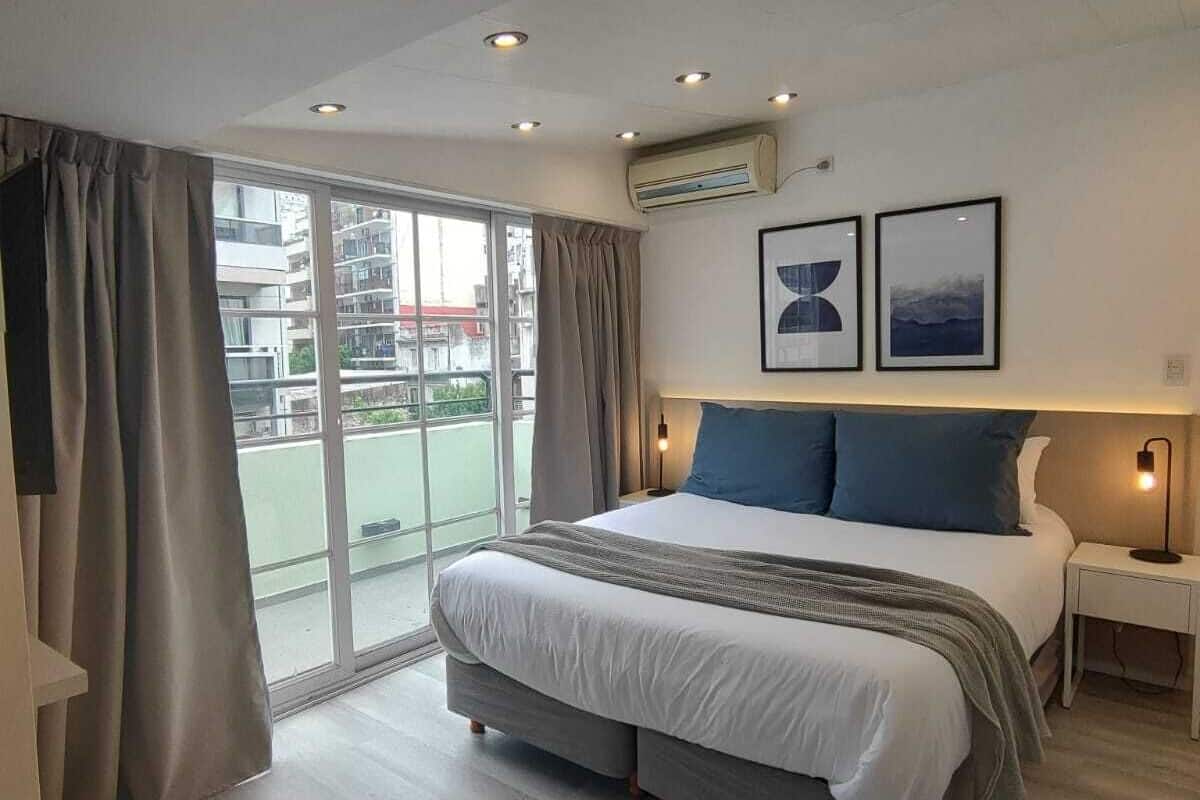 A modern bedroom with a large bed, a sliding glass door to a balcony, and two framed pictures on the wall.