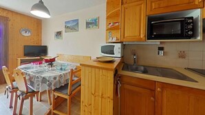 A compact kitchen with wooden cabinets, a microwave, a toaster oven, and a dining area with chairs and a table.