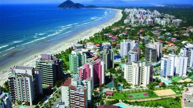 Un paisaje costero con edificios altos, una playa y montañas al fondo.