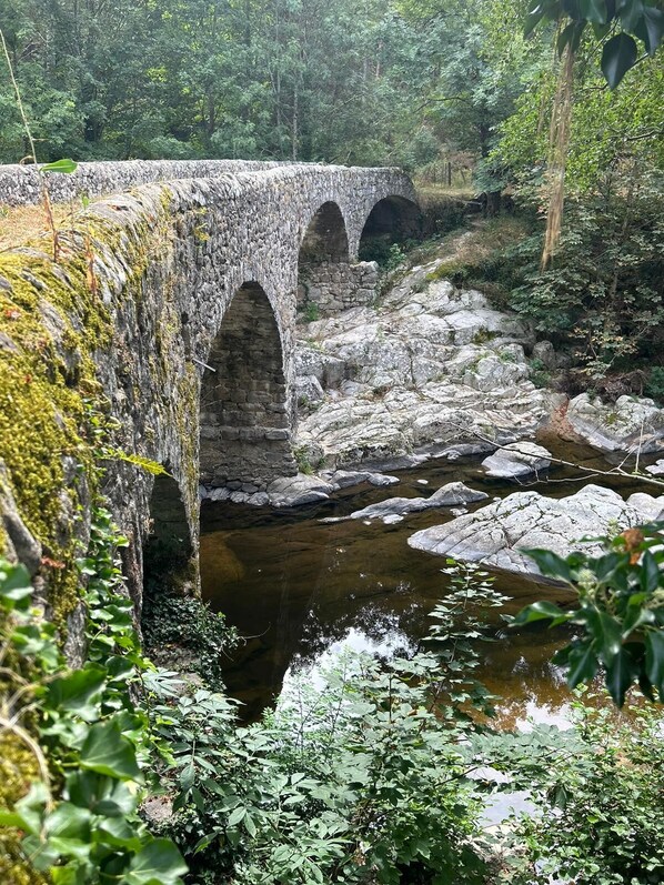 Un pont de pierre à trois arches enjambant une rivière, entouré d’une végétation luxuriante.
