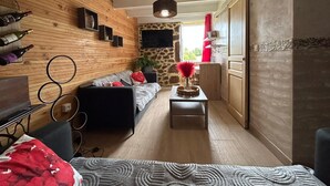 A narrow living room with a wooden wall, a sofa, a coffee table, and a TV mounted on the wall. - ARDECHE COUNTRY GITE OPEN ALL YEAR ROUND (Silhac)