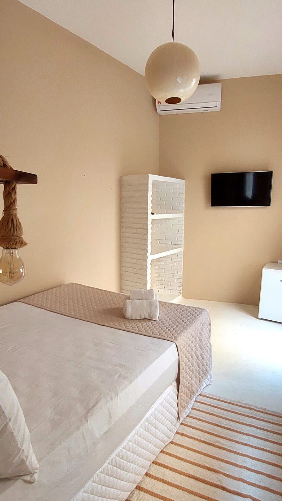 A bedroom with a bed, a TV, a wardrobe, and a hanging light fixture.
