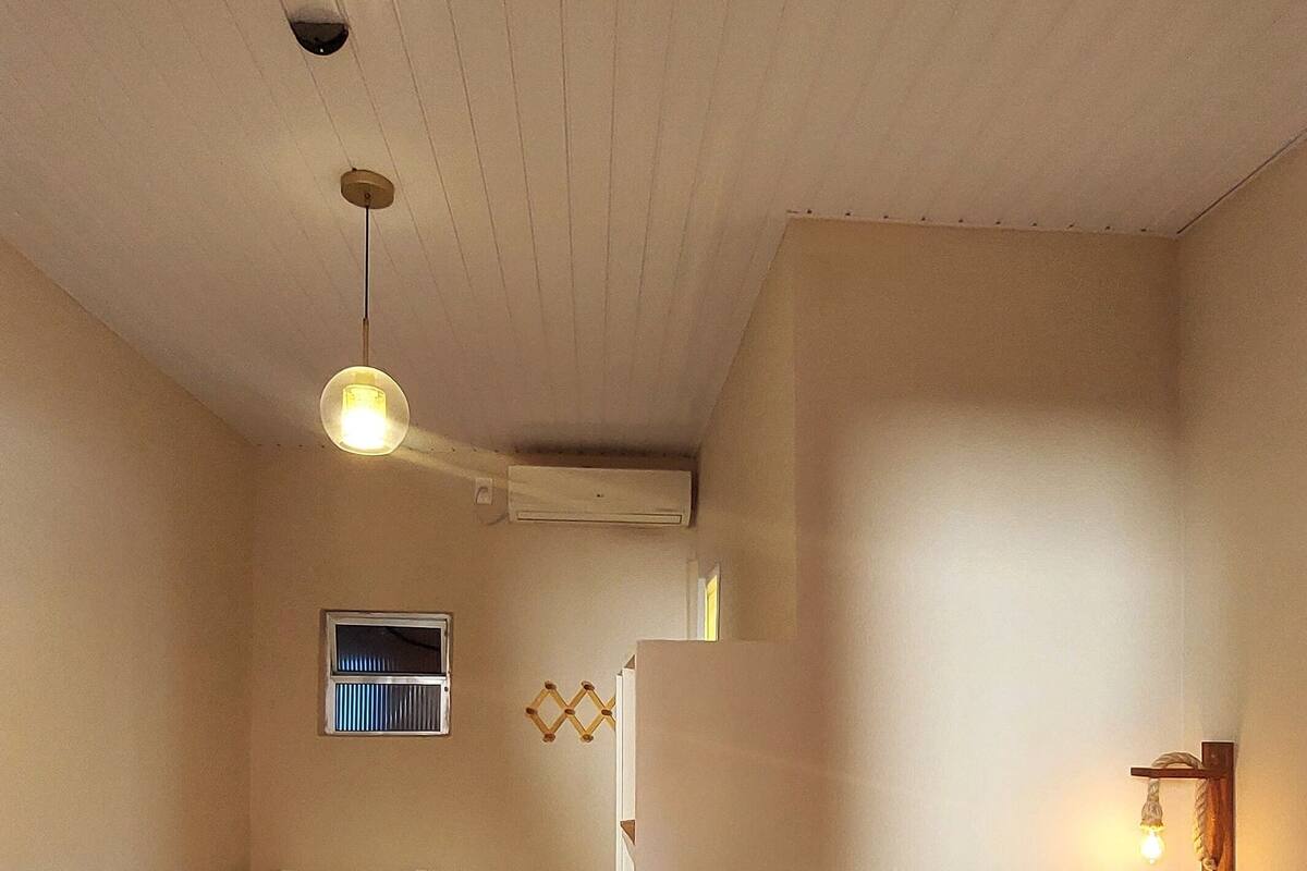 A room with two beds, a small table, a window with blinds, and a wall-mounted light fixture.