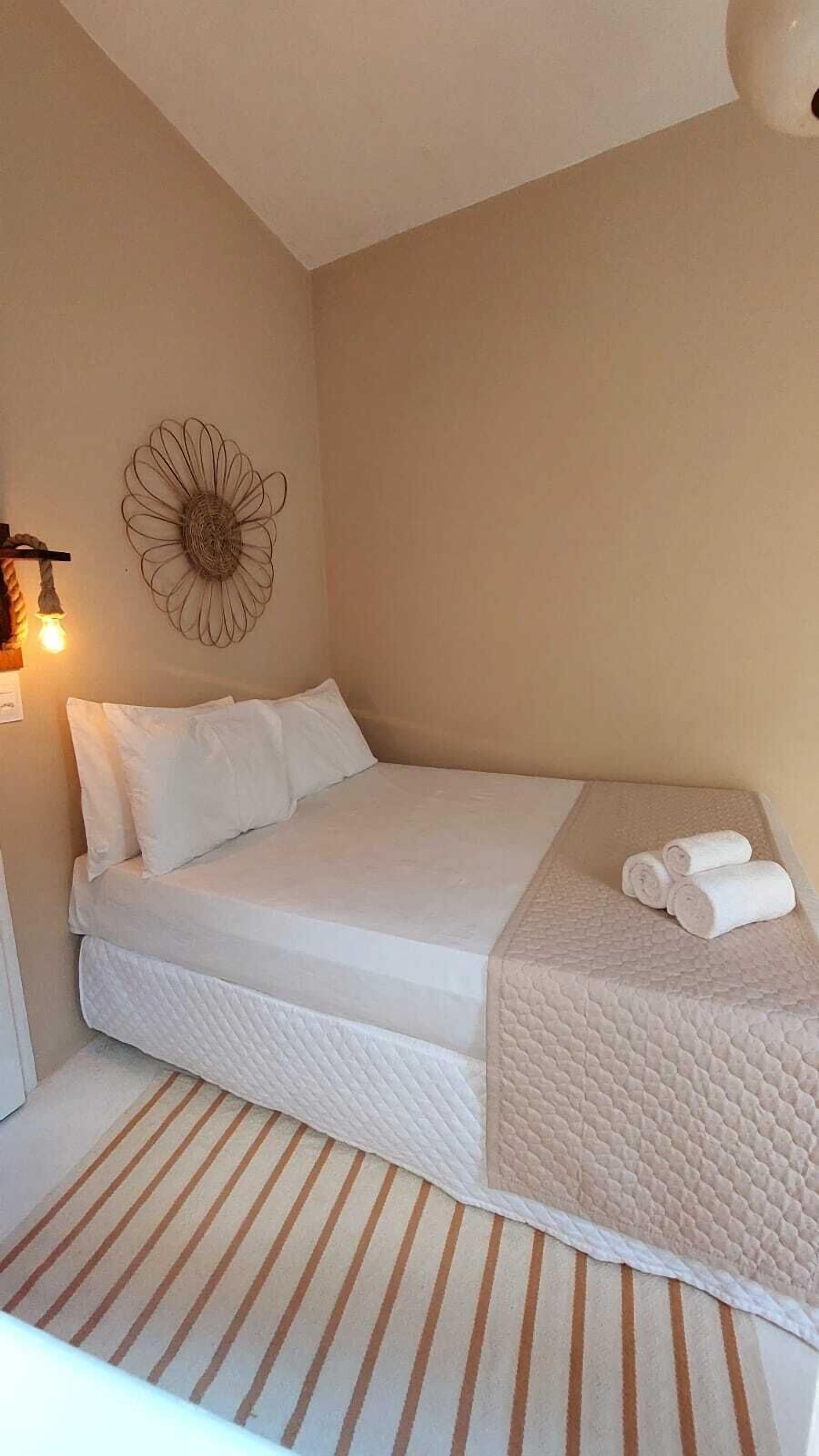 Una cama individual con ropa blanca, un adorno en la pared y un tapete a rayas.