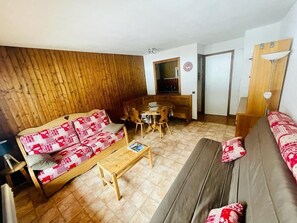 Een woonkamer met een wand van houten panelen, een bank, een salontafel en een eethoek met een tafel en stoelen.
