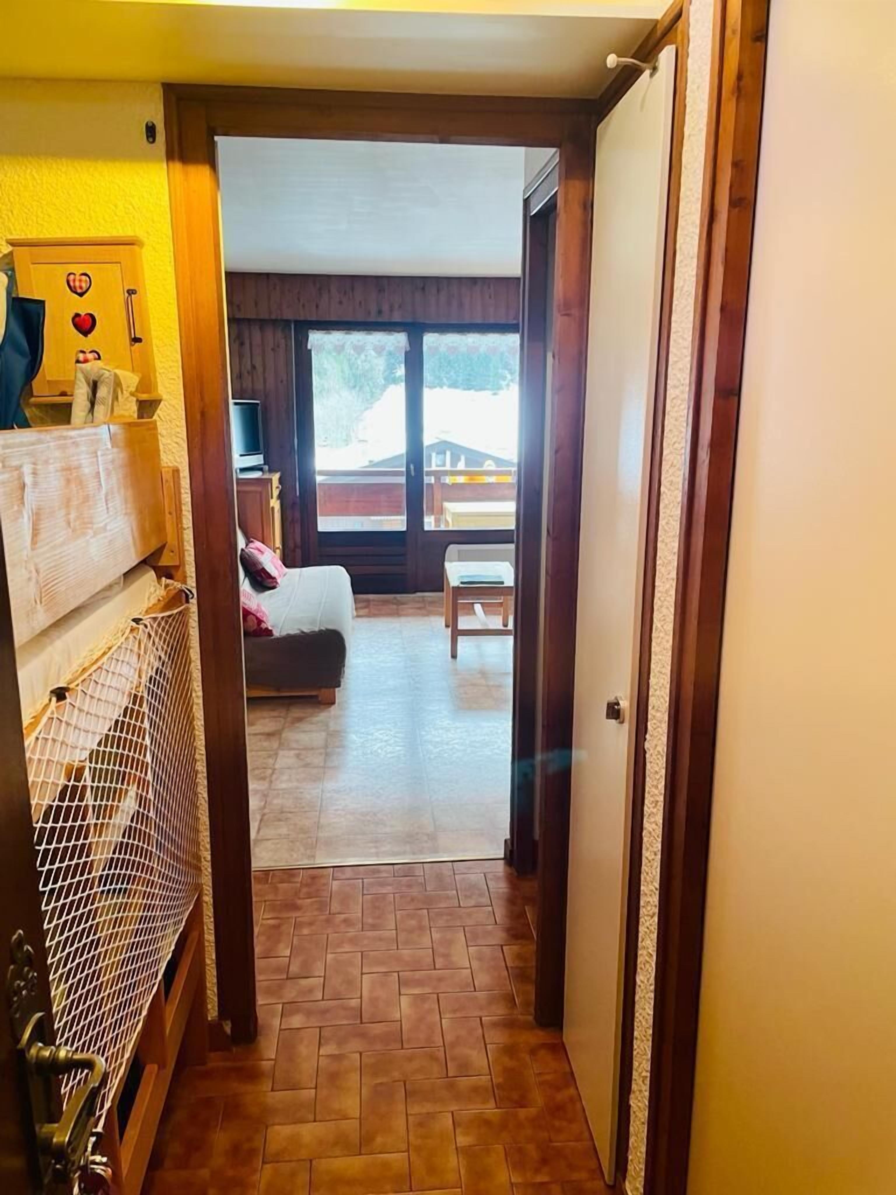 A hallway leading to a bedroom with a bed, a chair, and a small table.
