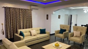 Una sala de estar con un sofá color beige, dos sillones, una mesa de centro y un comedor con sillas.
