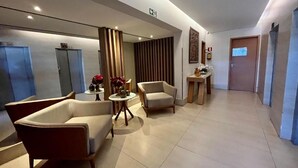 Un vestíbulo moderno con un sofá, sillones, una mesita con flores y un mostrador de recepción.