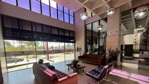 Un vestíbulo amplio con ventanas grandes, un sofá rojo, un sillón de cuero negro y una mesa de centro.