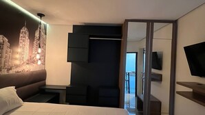 Habitación de hotel moderna con una cama grande, un cuadro de arte urbano en la pared, un televisor de pantalla plana y un balcón con vistas.