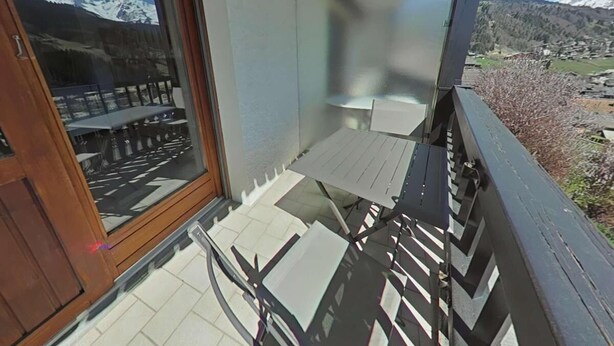 Een balkon met een tafel en stoelen, een houten leuning en een uitzicht op besneeuwde bergen.