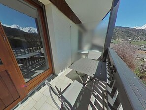 A balcony with a table and chairs, a wooden railing, and a view of snow-capped mountains.