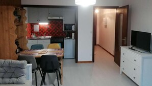 Een ruimtelijk ingerichte zithoek met een eethoek, kitchenette en een televisie op een dressoir.