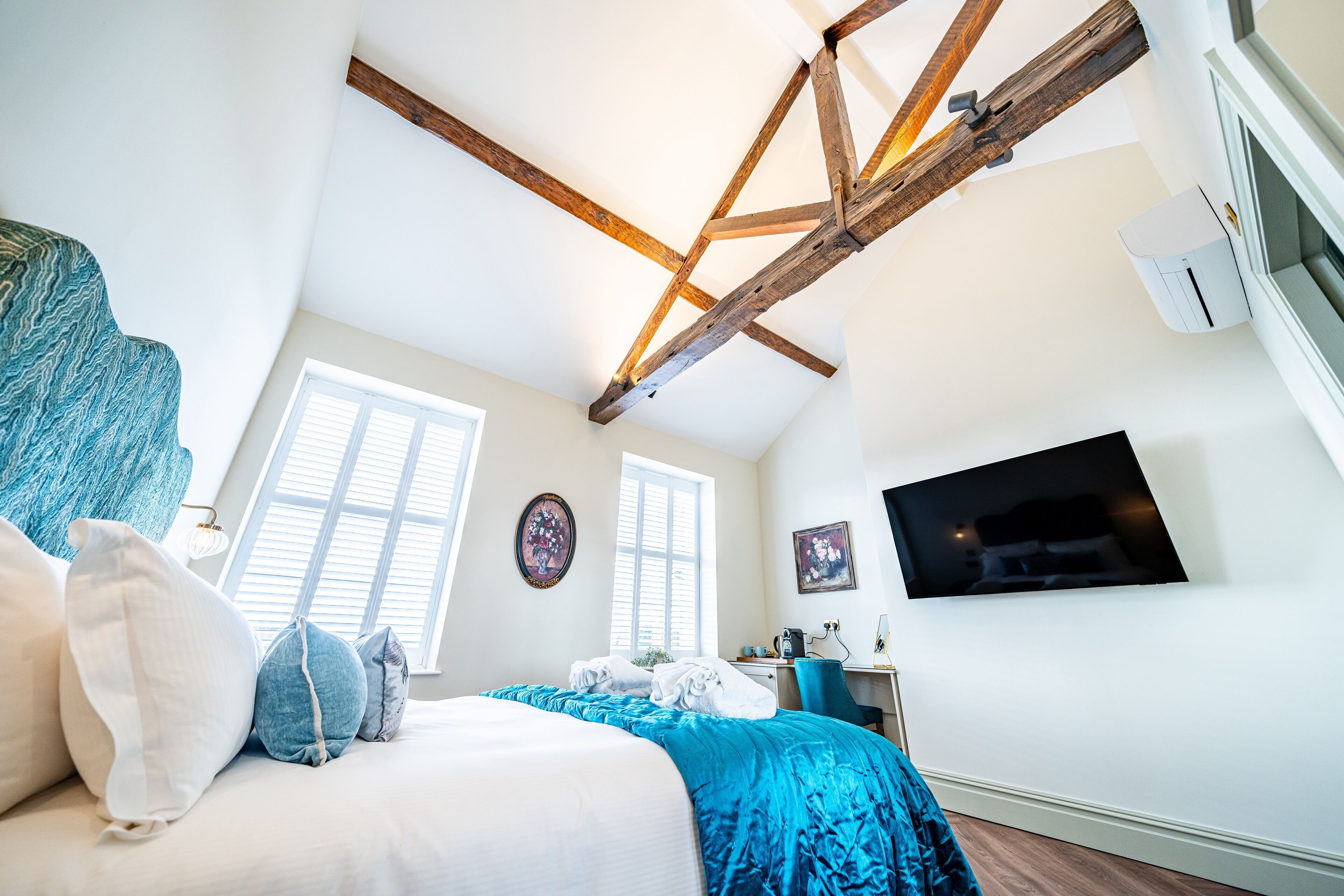 A bedroom with a bed, a desk, a TV, and a window.
