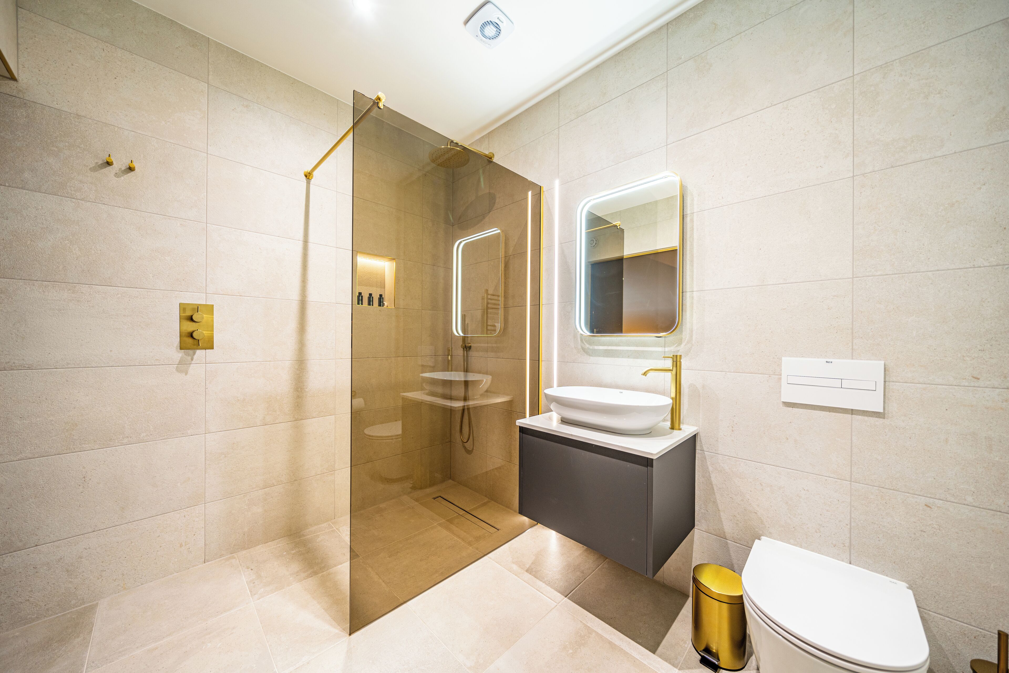 A modern bathroom with a glass-enclosed shower, a white sink, and a gold-colored trash bin.