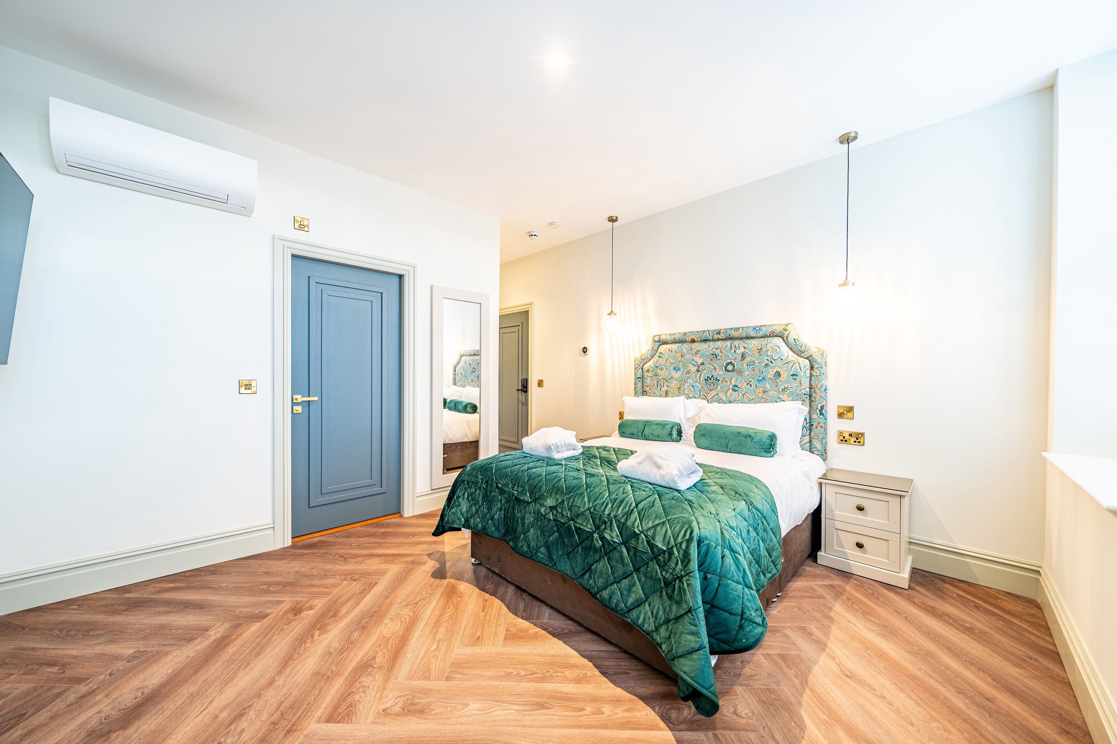 A bedroom with a large bed, a nightstand, a dresser, and a door.