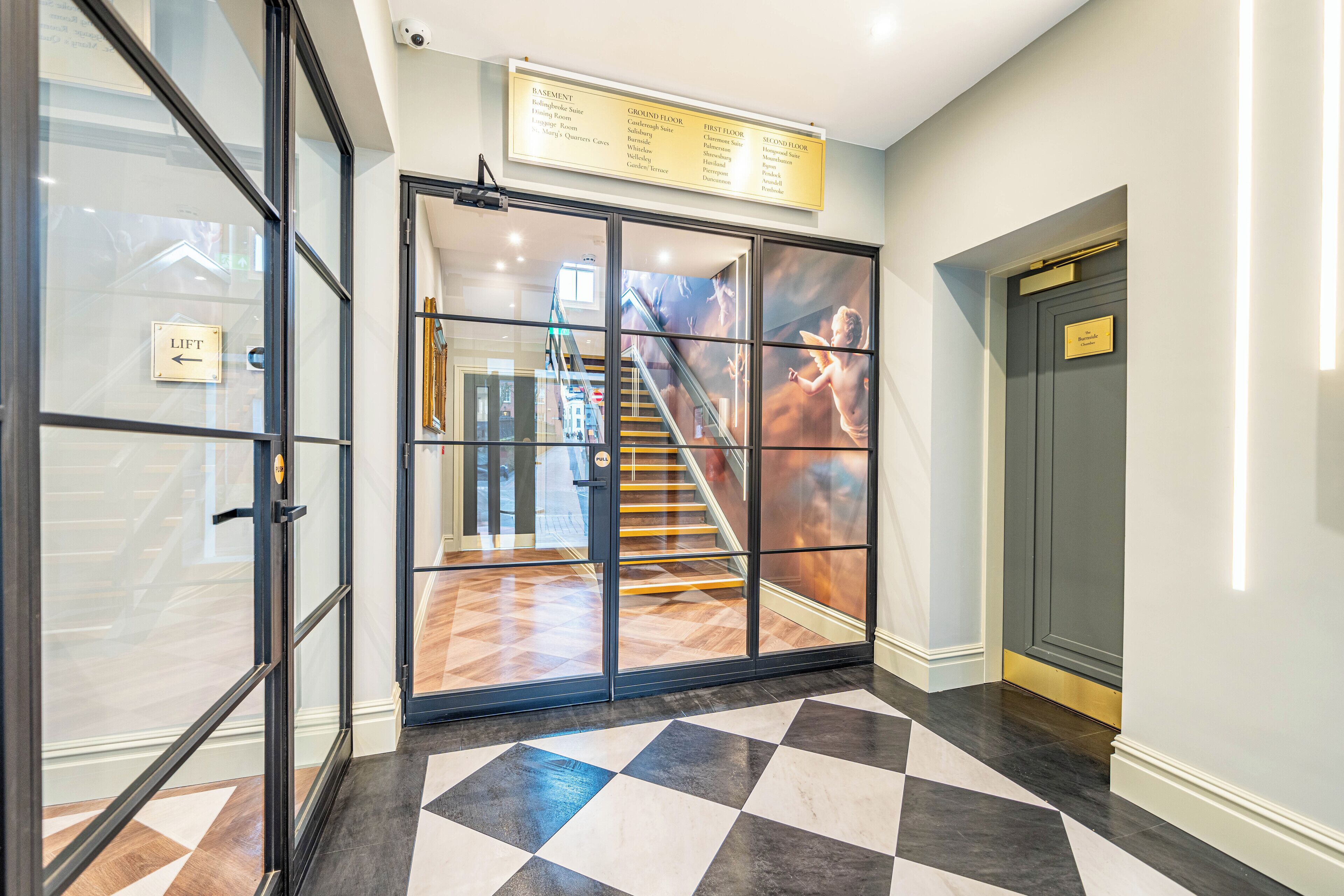 Ingresso di un hotel con reception, una scala e un cartello che indica il piano interrato e il piano terra.