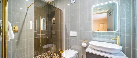 Une salle de bain moderne avec une douche à parois de verre, des toilettes blanches, un lavabo avec un robinet doré et des carreaux de sol à motifs.