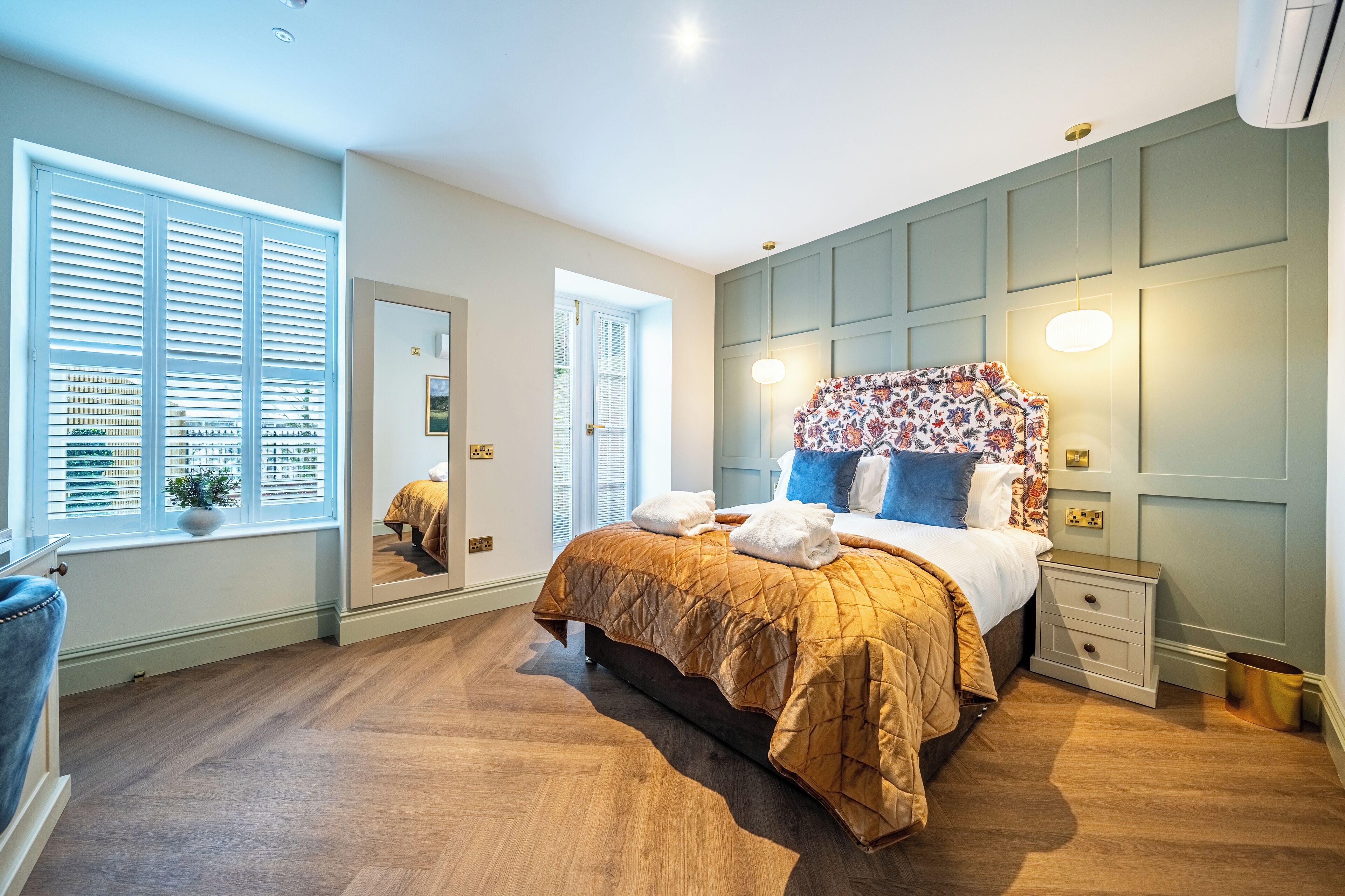 A bedroom with a large bed, a nightstand, a mirror, and a window with blinds.