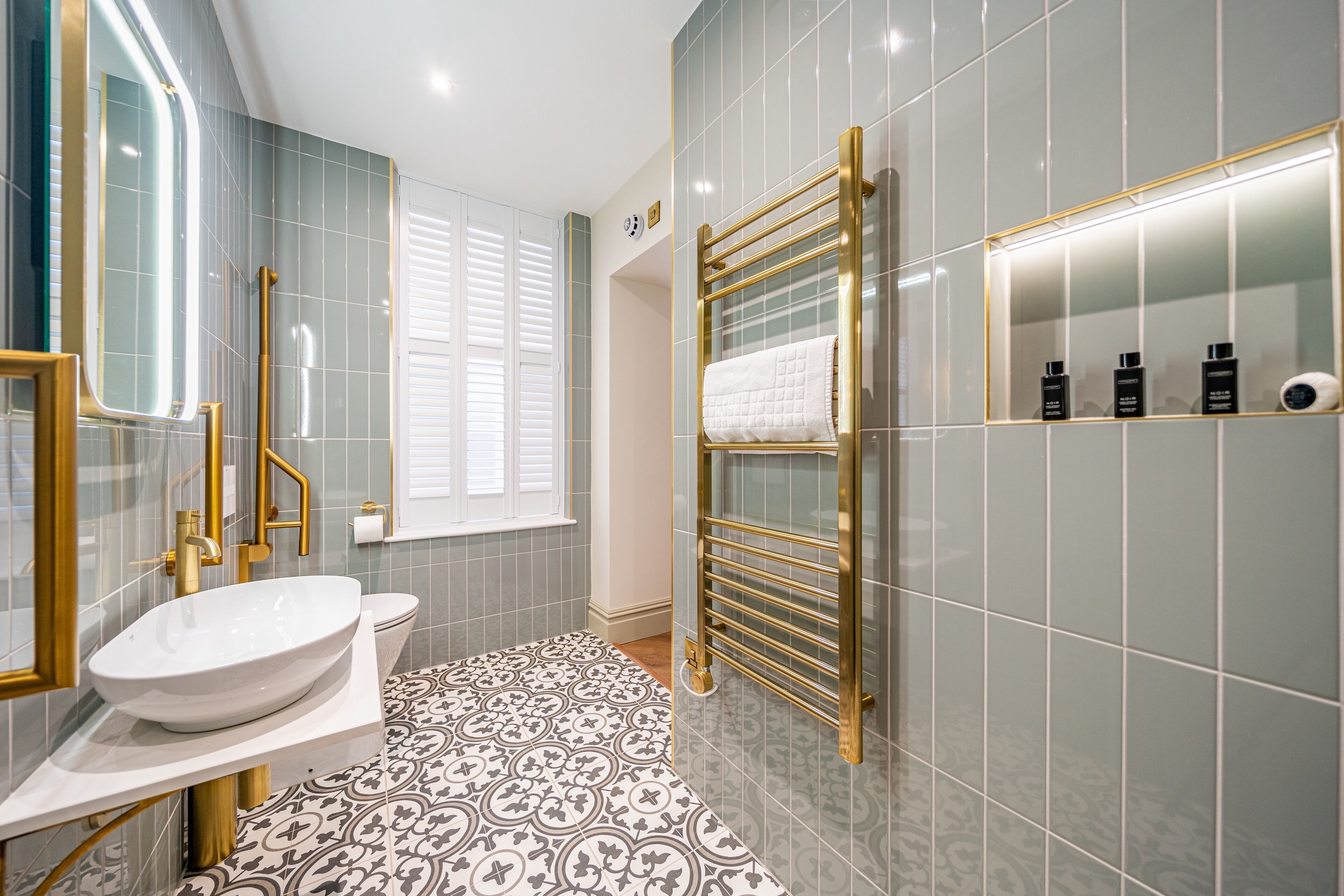 A modern bathroom with a white sink, gold fixtures, patterned floor tiles, and a glass-enclosed shower.