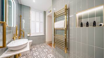 A modern bathroom with a white sink, gold fixtures, patterned floor tiles, and a glass-enclosed shower.