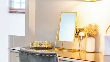 A modern desk with a gold lamp, a mirror, and a vase with dried flowers.