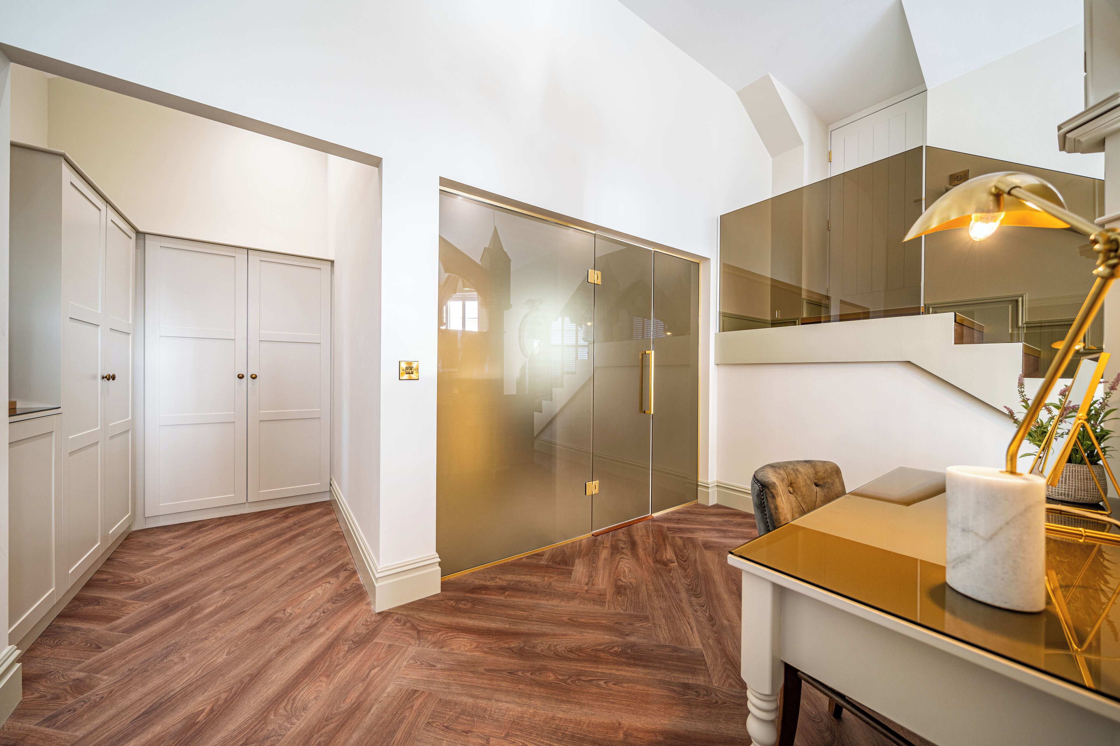 A modern interior with a wooden floor, a glass door leading to a staircase, and a table with a lamp.