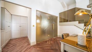 A modern interior with a wooden floor, a glass door leading to a staircase, and a table with a lamp.