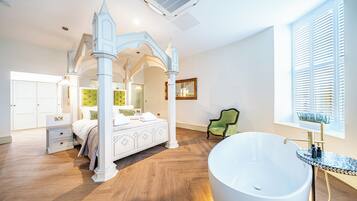 Una camera da letto con un letto a baldacchino, una vasca da bagno freestanding ampia e una poltrona verde.