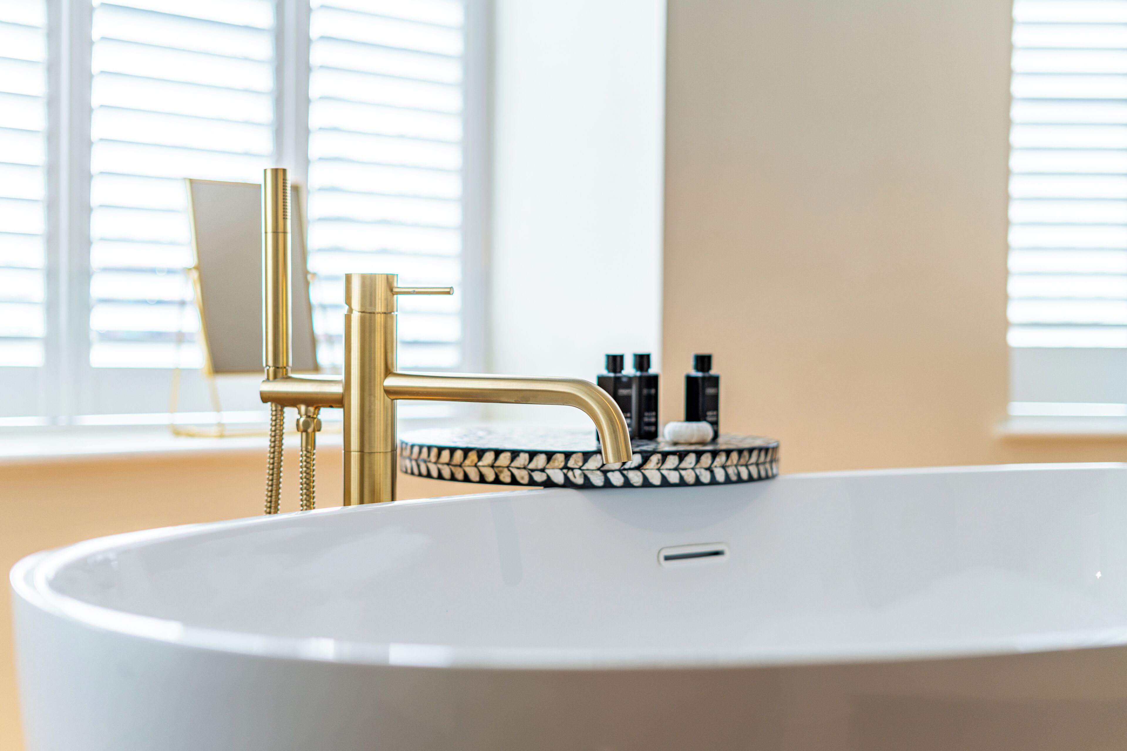 Ein modernes Badezimmer mit einer weißen Badewanne, goldenen Armaturen und einer dekorativen Fliesenleiste.
