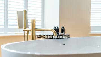 Ein modernes Badezimmer mit einer weißen Badewanne, goldenen Armaturen und einer dekorativen Fliesenleiste.