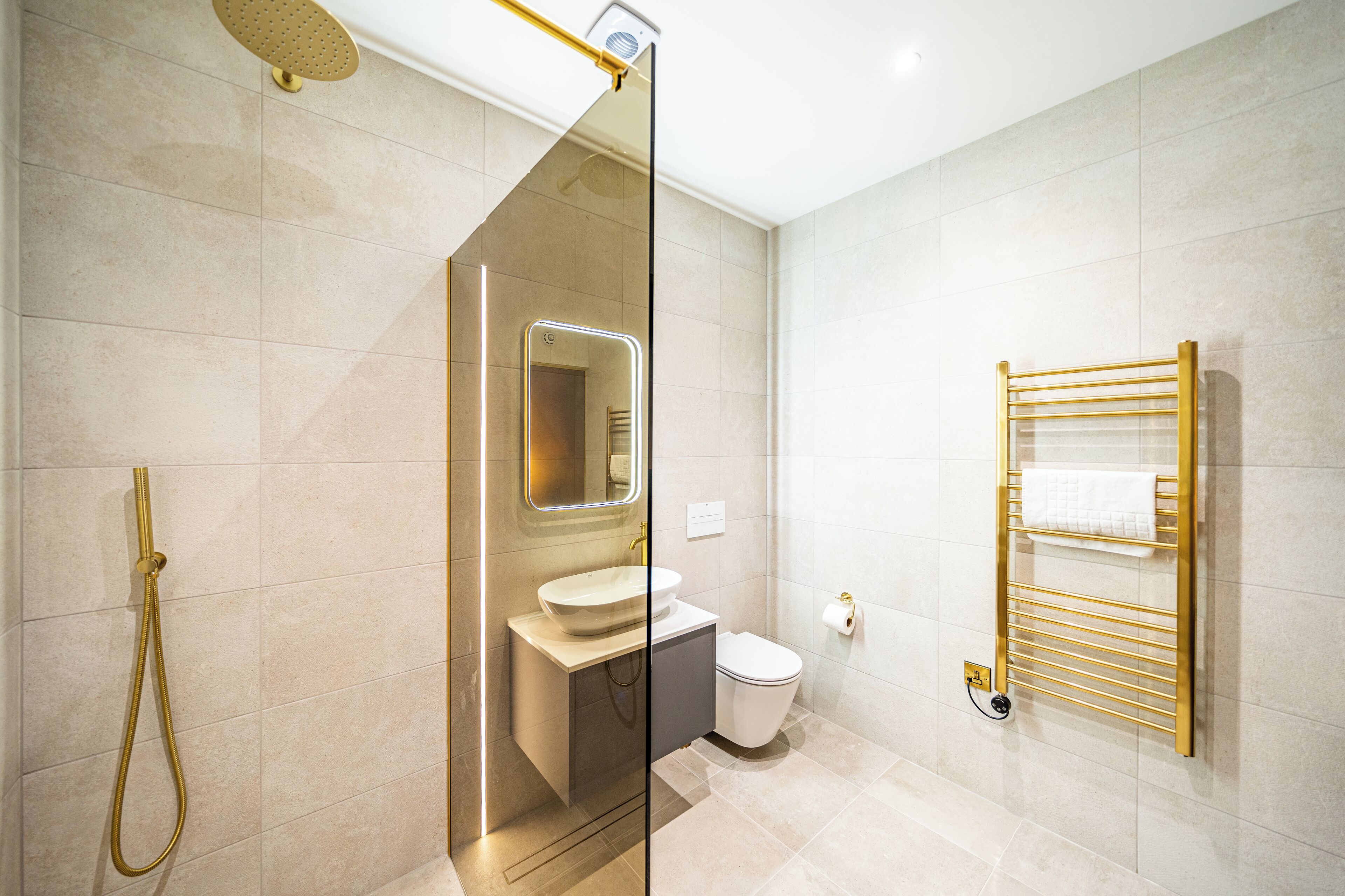 Un bagno moderno con doccia vetrata, lavandino bianco, WC e porta asciugamani dorato.