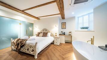Ein geräumiges Schlafzimmer mit einem großen Bett, einem separaten Schreibtisch, einer Badewanne und einer Duschkabine aus Glas.