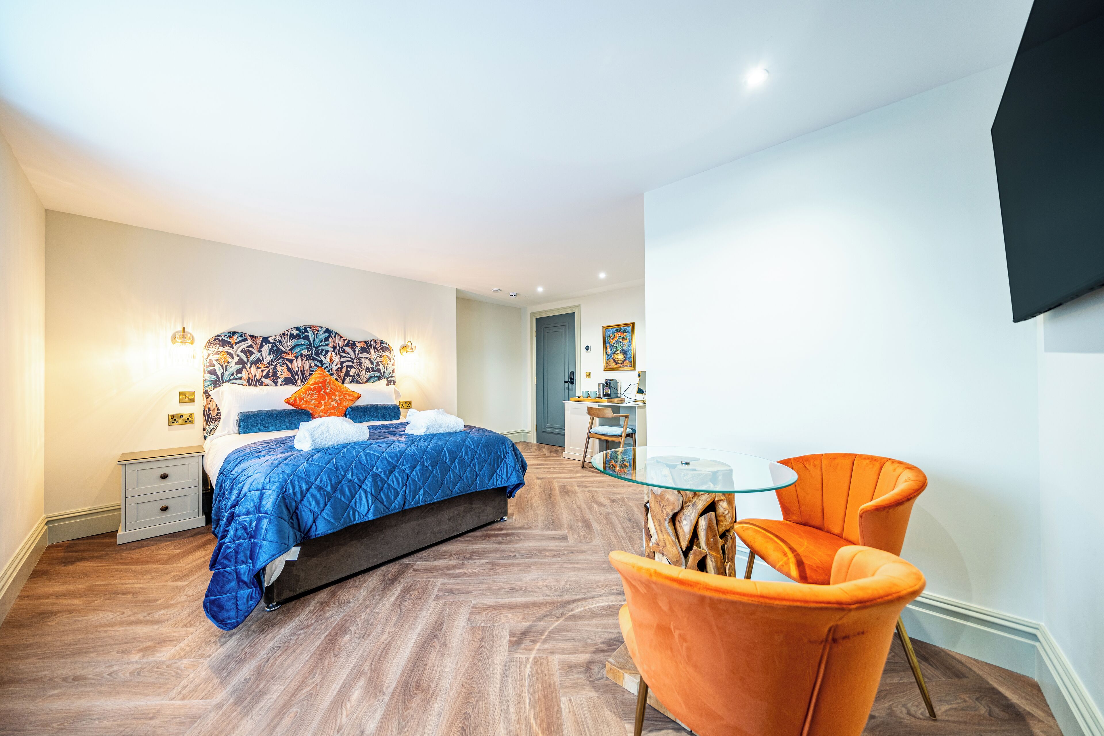 A modern bedroom with a bed, a nightstand, a glass coffee table, and an orange chair.