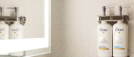 A bathroom with a modern sink, a mirror, and two Dove hand soap dispensers mounted on the wall.