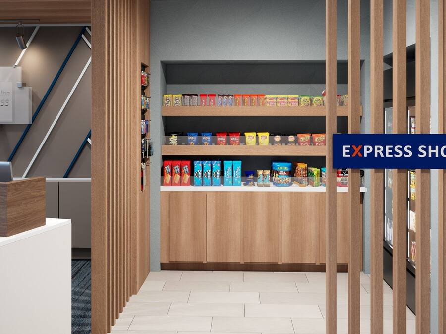 Un pasillo moderno de hotel con un mostrador de recepción de madera, una escalera y un bar de aperitivos con diversos productos envasados.