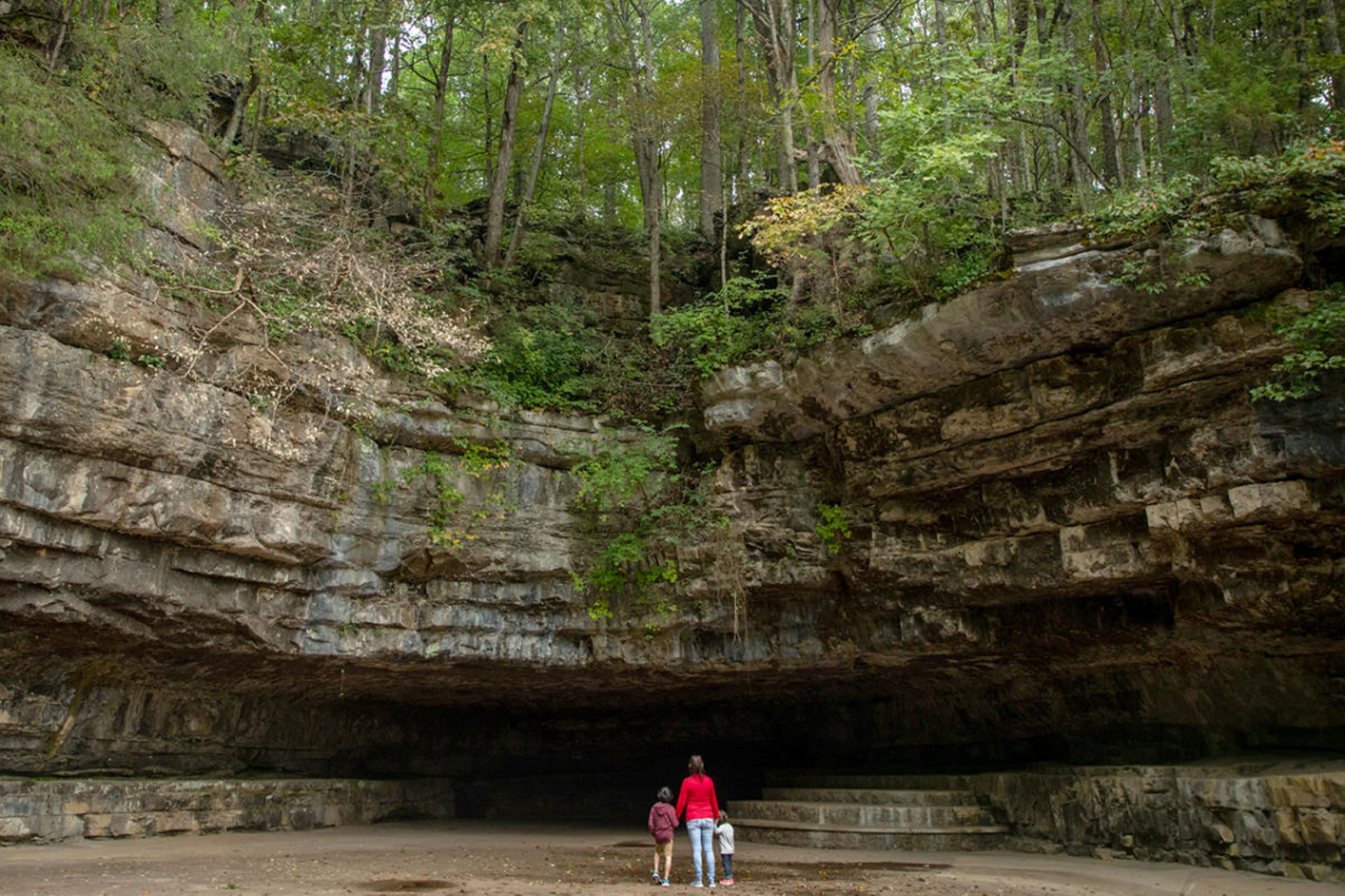 A natural cave formation with a person and two children standing at the entrance.