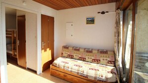 A cozy room with a wooden ceiling, a patterned sofa, a door, and a window with curtains.