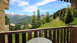 A balcony with a view of a mountainous landscape, including snow-capped peaks and a forested valley.