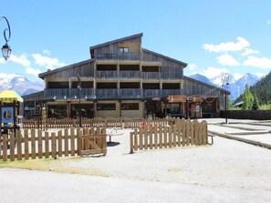 A multi-story building with balconies, a wooden fence, and a mountainous backdrop. - 10m from ski slopes, 4th floor, view mountain, balcony, tv, ski locker, 23m², Auris en Oisans (Auris)