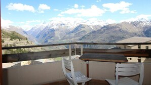 Een balkon met een tafel en twee stoelen, met uitzicht op een bergachtig landschap met besneeuwde toppen.
