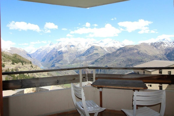 A balcony with a table and two chairs, overlooking a mountainous landscape with snow-capped peaks. - 10m from ski slopes, 4th floor, view mountain, balcony, tv, ski locker, 23m², Auris en Oisans (Auris)