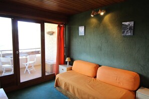 A bedroom with a bed, a nightstand, a lamp, and a view of an outdoor area with chairs and a table. - 10m from ski slopes, 4th floor, view mountain, balcony, tv, ski locker, 23m², Auris en Oisans (Auris)