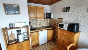 Une cuisine compacte avec des meubles de rangement en bois, un four à micro-ondes, une machine à café et un petit évier.