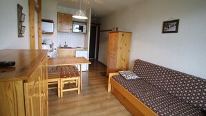 A compact kitchen with wooden cabinets, a dining table, and a bench. There is a small kitchenette with a microwave and a sink. A wooden bench with a patterned cushion is against the wall. - 300m from ski slopes, Ground floor, view valley, balcony, tv, ski locker, 19m², Auris en Oisans (Auris)