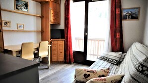 Een gezellige kamer met een bed, een bureau en een stoel. Er zijn houten kasten en een raam met gordijnen.